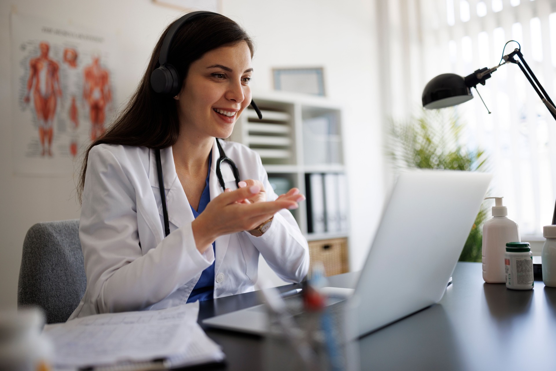 Smiling female doctor in her office, using a laptop to give online consultations while wearing a headset